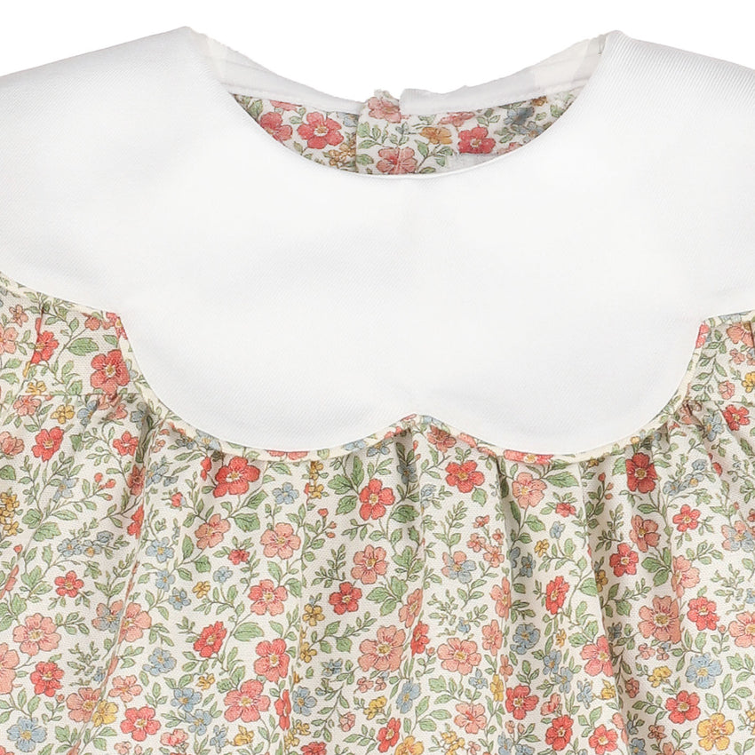 Close-up of a dress neckline with a solid scalloped white collar and a ruffled floral skirt featuring red, pink, green, and yellow flowers on a cream background.