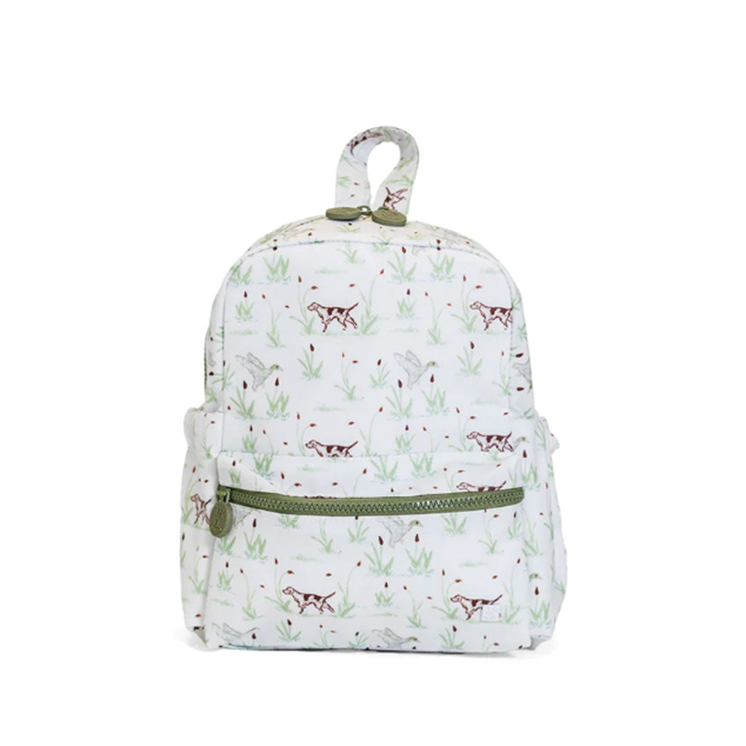 A white backpack featuring an all-over print of hunting dogs, marsh grass, and red berries, accented with olive green zippers and top loop.