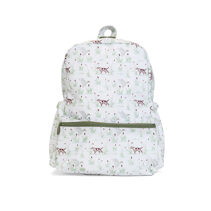 A white backpack with an all-over print of small brown dogs and green leaves, featuring a green zipper on the front pocket and a gray top handle.