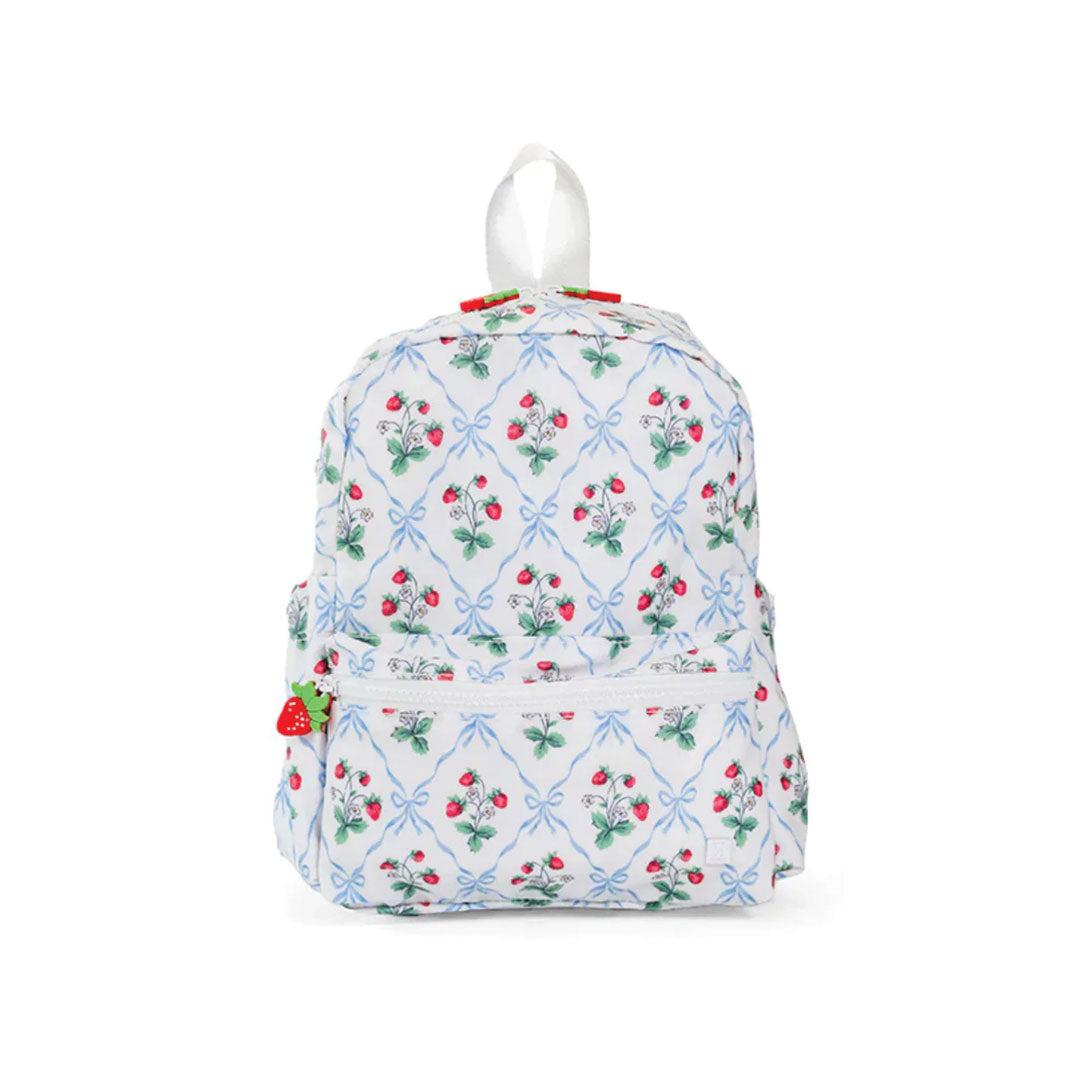 A small backpack with a white background and a repeating pattern of red strawberries, green leaves, and light blue bows. It features a top carrying handle, a front zippered pocket, and small strawberry-shaped zipper pulls on the sides.