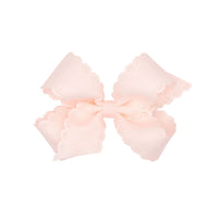 Rose colored bow with scalloped edges on a white background.
