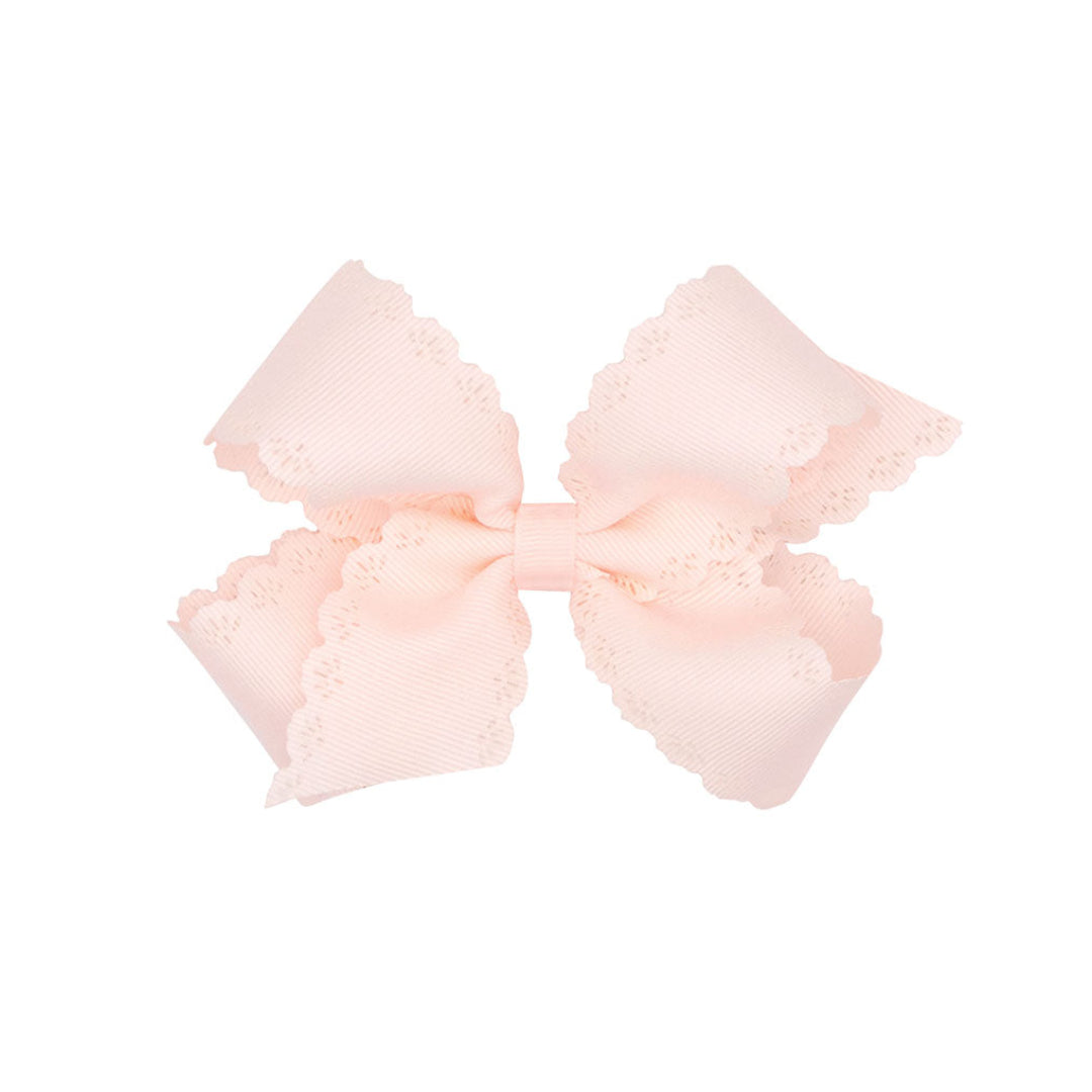 Rose colored bow with scalloped edges on a white background.
