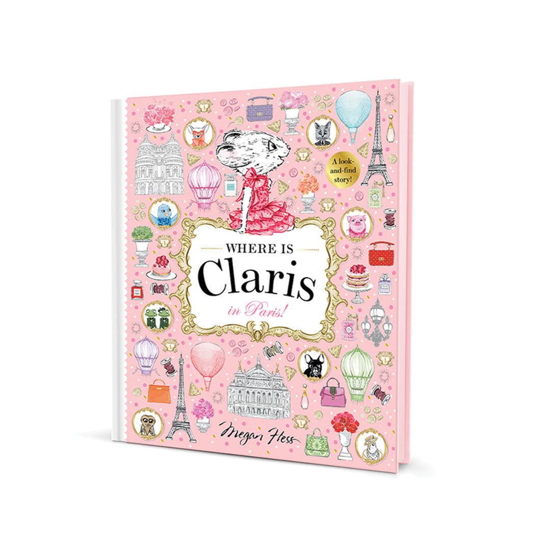 A pink hardcover book titled 'Where Is Claris in Paris!' with illustrated Parisian motifs such as the Eiffel Tower, hot air balloons, and postcards on the cover, photographed on a clean white background.