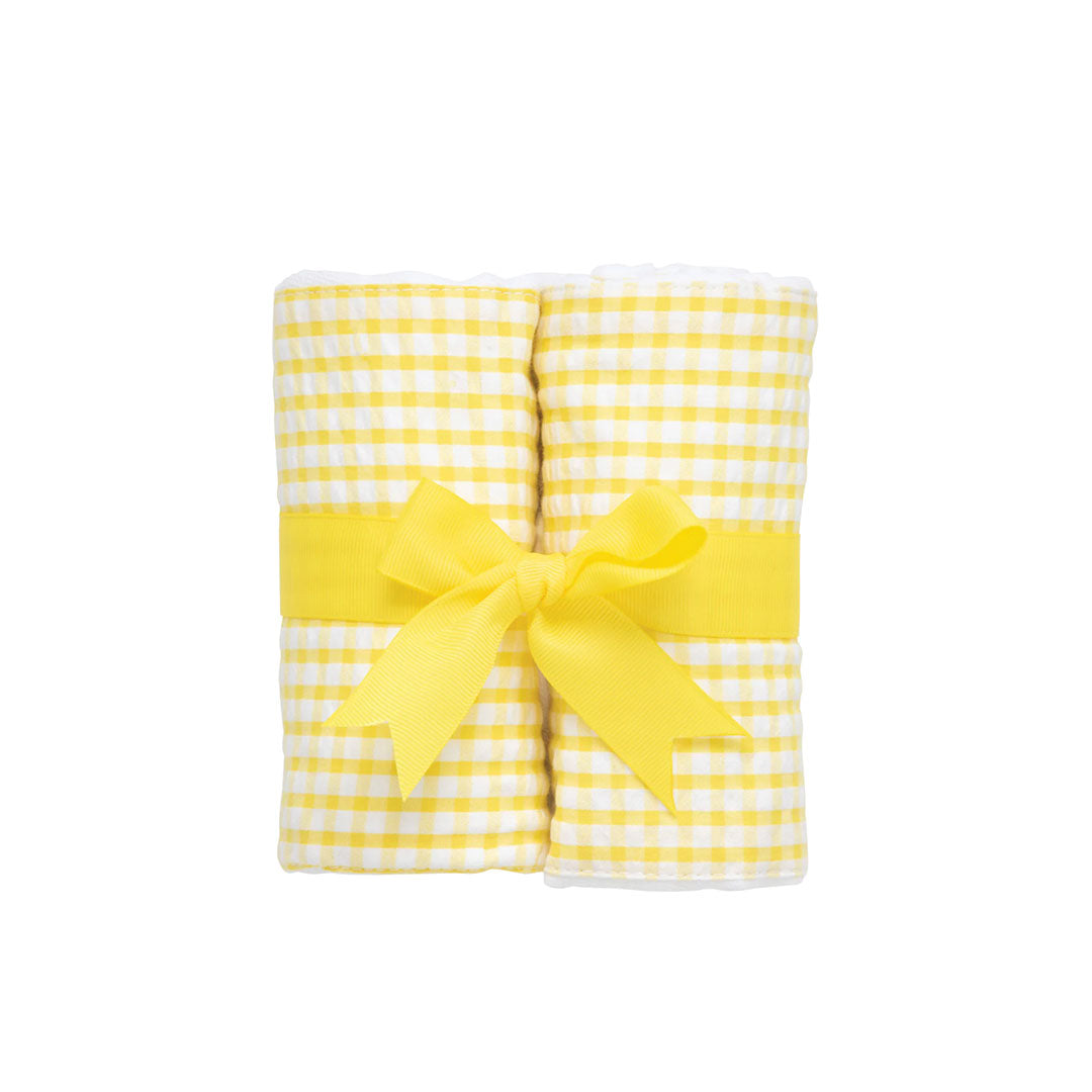 Two rolled checkered burp cloths - yellow and white check - with a yellow bow on a white background.